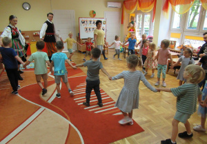 Dzieci tańczą w kole podczas koncertu, z Panią i Panem w strojach łowickich.