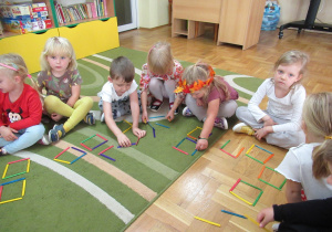 Dzieci układają na podłodze kwadraty z patyczków.
