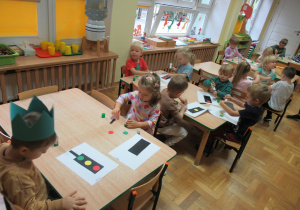 Dzieci siedzą przy stolikach i wykonują prace plastyczne - sygnalizatory.