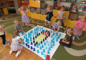 Dzieci układają kolorowe kubeczki na macie do kodowania.