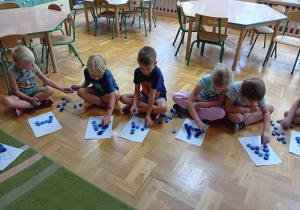 Dzieci układają kontur litery A za pomocą plastikowych nakrętek