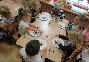 Dzieci siedzą przy stolikach i wyklejają liście z plasteliny.