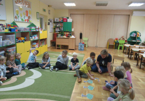 Dzieci siedzą w kole, chłopiec układa owoce z papieru.