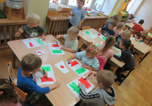 Dzieci siedzą przy stolikach i malują farbami flagę Włoch.