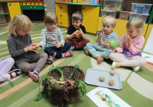 Dzieci siedzą na dywanie i oglądają warzywa.