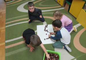 Dzieci na dywanie układają kasztany.