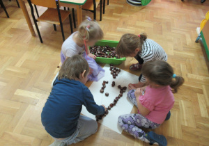 Dzieci wypełniają kształt marchewki narysowanej na kartce kasztanami.