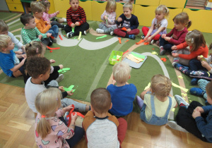 Dzieci siedzą w kole na dywanie i rozdzierają kolorowe paski na małe kawałki.