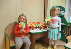 Dziewczynki prezentują prace plastyczne - jesienne drzewka z rolek.