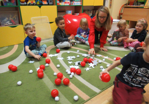 Dzieci zbierają czerwone piłeczki podczas warsztatów.