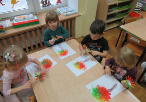 Dzieci siedzą przy stoliku i malują drzewa.