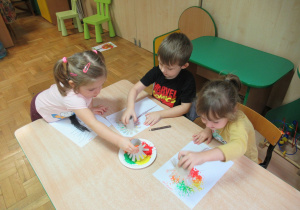 Dzieci przy stoliku malują jesienne drzewa.