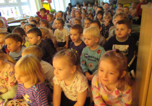 Dzieci siedzą na podłodze i oglądają przedstawienie teatralne.
