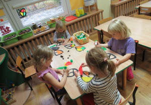 Dzieci siedzą przy stole i wykonują witraże - jesienne liście.