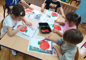Dzieci przy stoliku malują jabłka