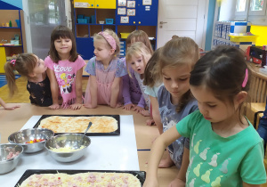 Dzieci uzupełniają ciasto pizzy składnikami