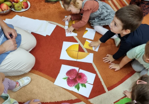 Dzieci siedzą na dywanie i układają puzzle z obrazkami owoców.