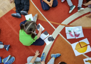 Przedszkolaki siedzą na dywanie i układają puzzle z obrazkami owoców.