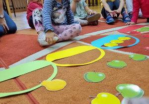 Dzieci siedzą na dywanie i układają obrazki z koszyczkami i owocami.