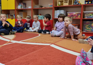 Dzieci siedzą na dywanie i słuchają.