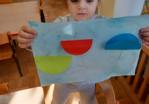 Dziewczynka pokazuje swoją pracę plastyczna: "Parasolki".