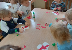 Dzieci wyklejają czerwonym papierem serce.
