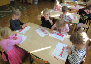Dzieci siedzą przy stolikach i wyklejają plasteliną flagę Polski.