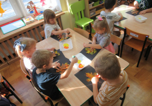Dzieci siedzą przy stolikach i wykonują pracę plastyczną.