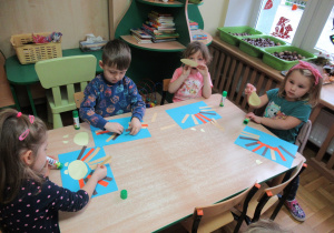 Dzieci przy stolikach przyklejają paski na kartkę.