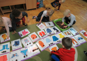 Dzieci ukłądają obrazki i kasztany na podłodze.