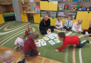 Dzieci z panią siedzą na dywanie podczas zajęć z języka angielskiego.