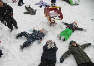 Dzieci leżą na śniegu i robią "aniołki".