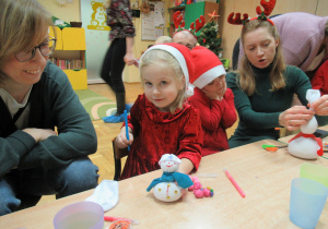 Dziewczynki z rodzicami wykonują bałwanki podczas warsztatów świątecznych.