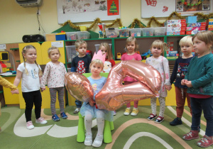 Dzieci świętują urodziny koleżanki, jubilatka siedzi na krzesełku i trzyma w rękach balony.