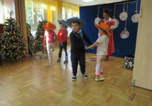 Dzieci w kapeluszach tańczą w parach.