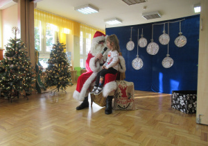 Dziewczynka siedzi Mikołajowi na kolanach.