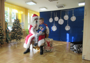 Chłopiec siedzi Mikołajowi na kolanach.