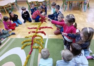 Dzieci układają kształt choinki z kolorowych łańcuchów świątecznych
