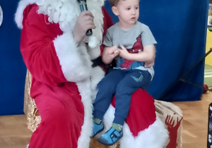 Chłopiec siedzi na kolanach pana przebranego za Świętego Mikołaja.