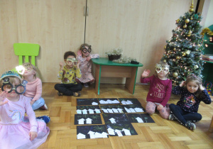 Dzieci siedzą na podłodze i prezentują prace plastyczne.