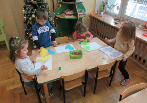 Dzieci przy stoliku wykonują pracę plastyczną - rękawiczki.