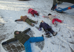 Dzieci leżą na śniegu i robią "aniołki".