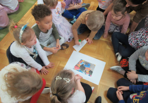 Dzieci siedzą na podłodze i układają obrazek z części.