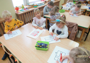 Dzieci siedzą przy stoliku i kolorują kredkami flagi Danii.