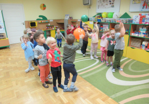 Dzieci stoją w dwóch rzędach i podają sobie balony.