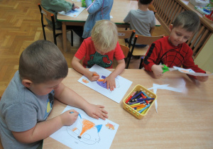 Dzieci siedzą przy stoliku, kolorują i wycinają.