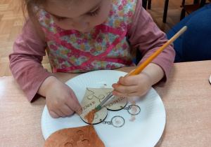 Dziewczynka maluje farbami drewniane serce.