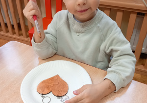 Chłopiec maluje farbami drewniane serce.