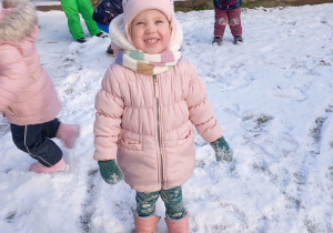 Dziewczynka stoi na śniegu i się uśmiecha.