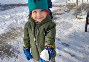 Chłopiec trzyma kulkę śniegu na placu zabaw.